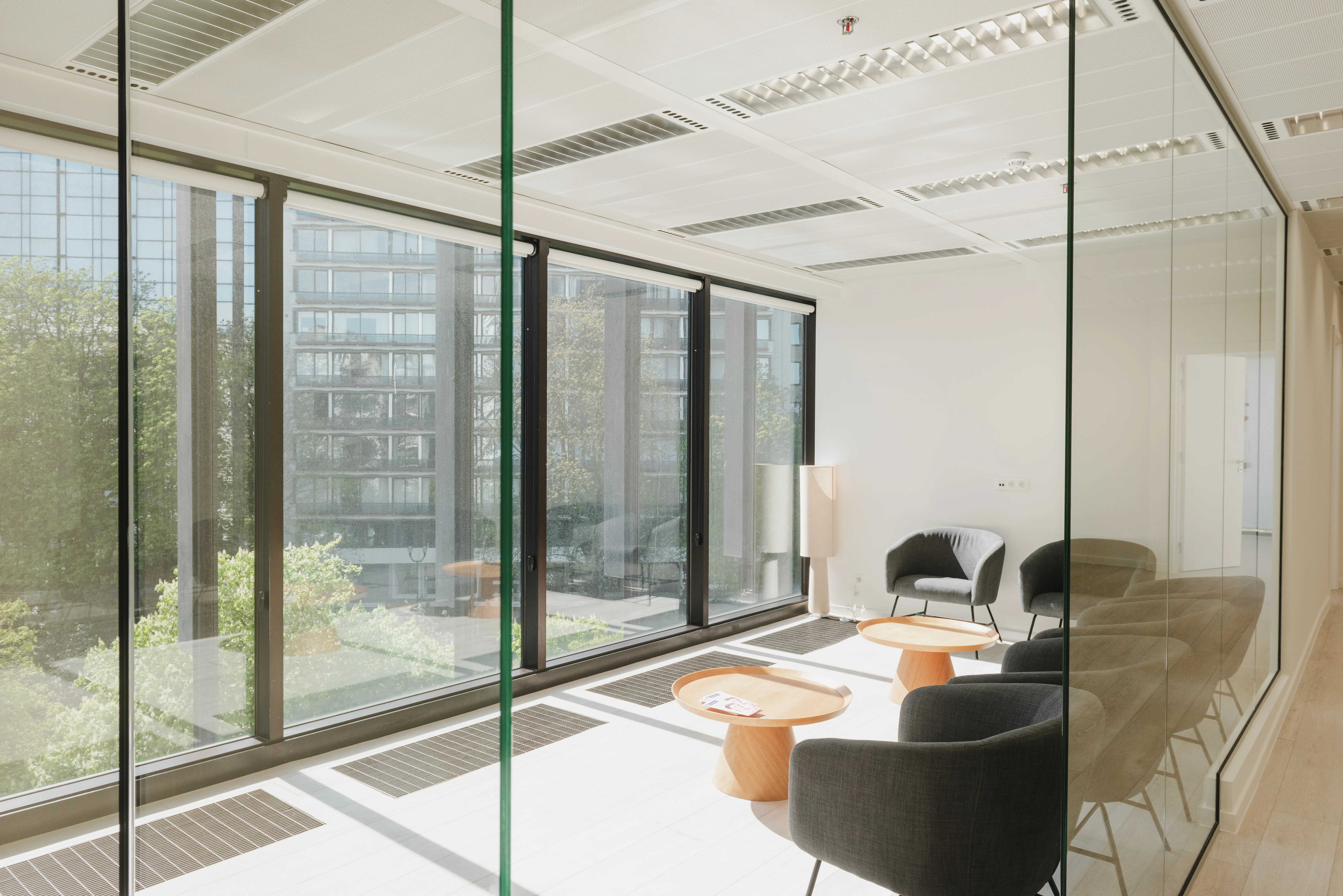 Daylit waiting area with armchairs behind a glass wall